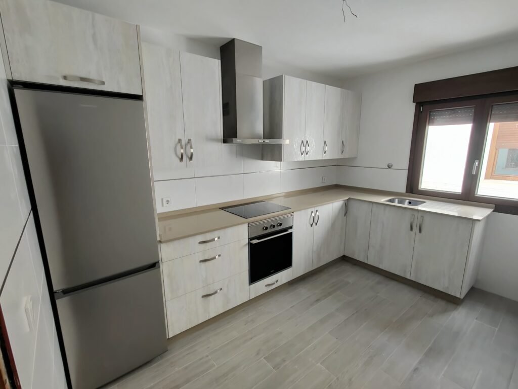 Cocina en L, muebles claros y electrodomésticos en acero inoxidable.